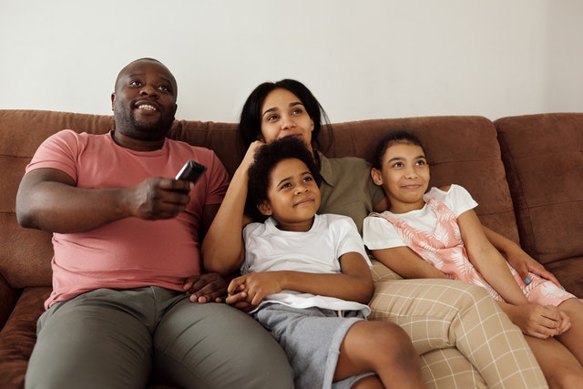family sitting on a brown couch watching TV